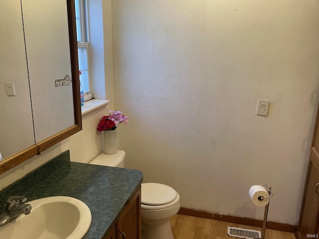 bathroom with visible vents, toilet, vanity, wood finished floors, and baseboards
