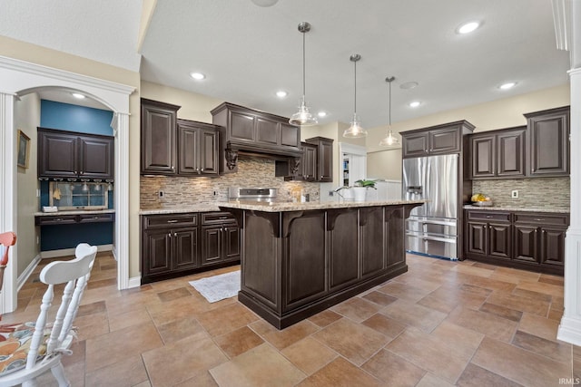 kitchen featuring dark brown cabinetry, stainless steel fridge, decorative backsplash, a kitchen island, and a kitchen bar