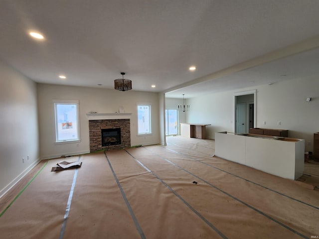 unfurnished living room featuring a stone fireplace, baseboards, a wealth of natural light, and recessed lighting