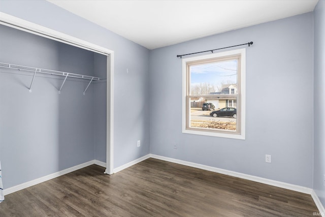 unfurnished bedroom with dark wood-style flooring, a closet, and baseboards