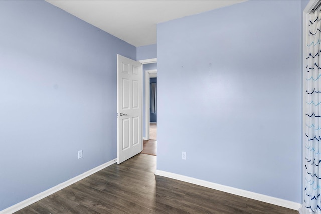 spare room featuring dark wood-type flooring and baseboards