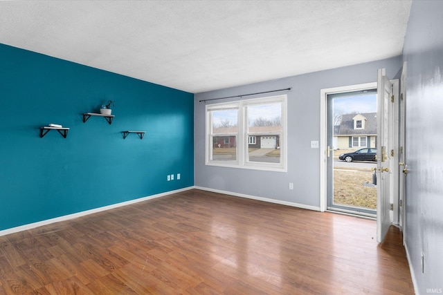 unfurnished room with a textured ceiling, baseboards, and wood finished floors