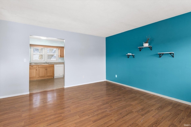 empty room featuring dark wood-style flooring, a sink, and baseboards