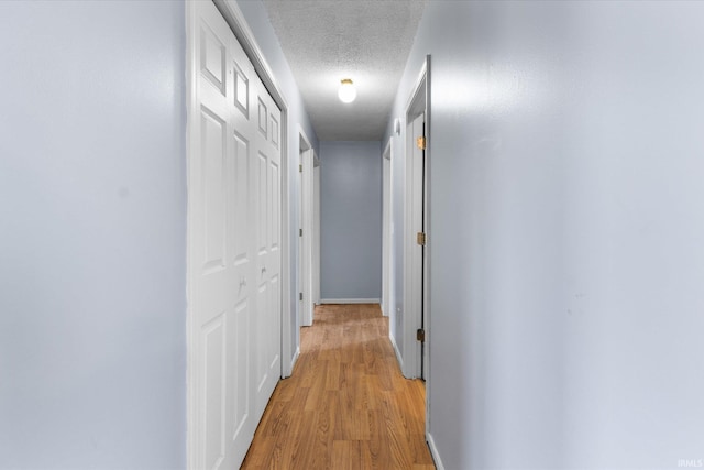 corridor with a textured ceiling, light wood-style flooring, and baseboards