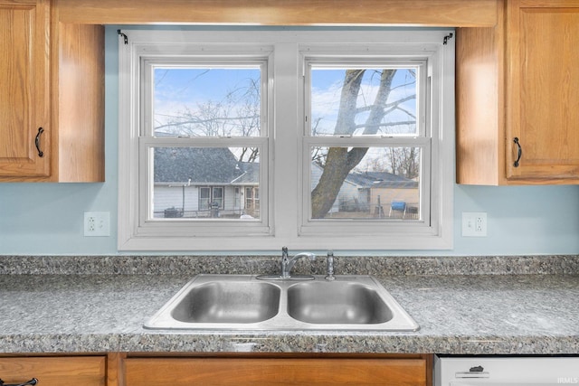 kitchen featuring brown cabinetry, a sink, and dishwashing machine