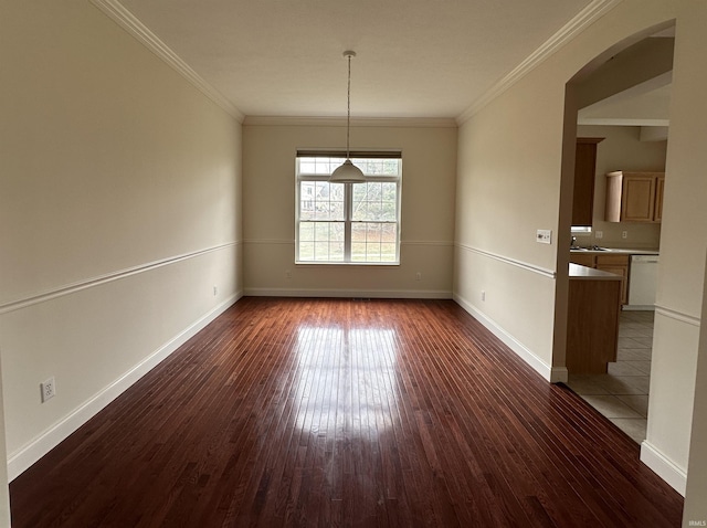 empty room with arched walkways, baseboards, dark wood finished floors, and crown molding