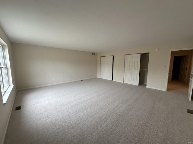 unfurnished bedroom with baseboards, light carpet, visible vents, and multiple closets