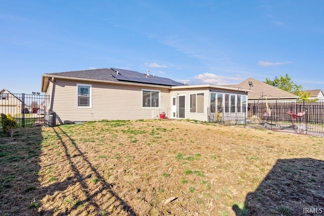 rear view of property featuring a sunroom, a lawn, solar panels, and fence