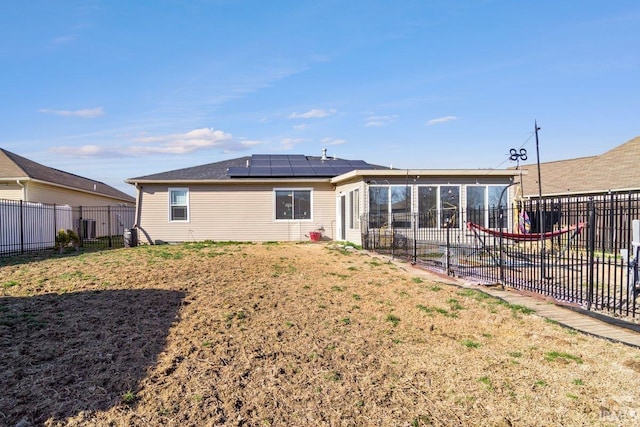 back of property with solar panels, a fenced backyard, a lawn, and a sunroom