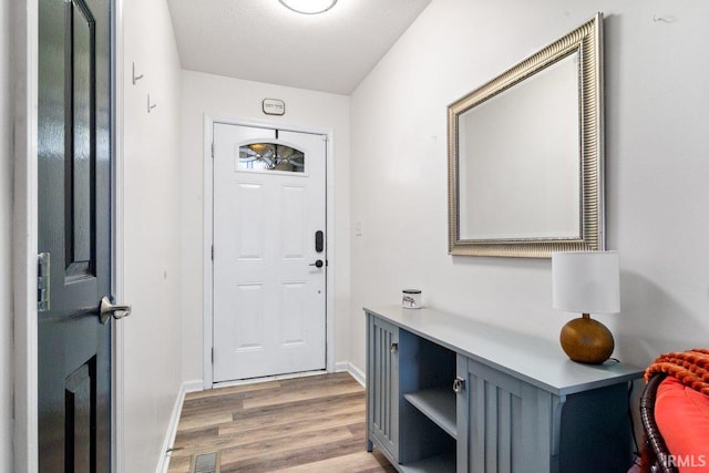 doorway to outside with visible vents, a textured ceiling, light wood-type flooring, and baseboards