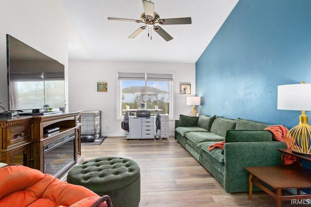 living room with a ceiling fan, wood finished floors, a fireplace, baseboards, and vaulted ceiling