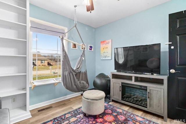 living area featuring visible vents, baseboards, wood finished floors, and a ceiling fan