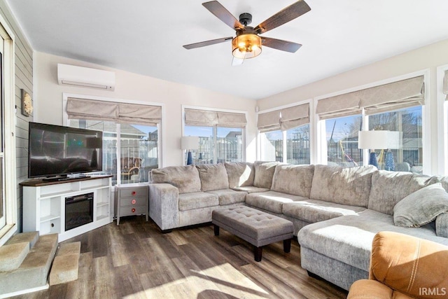 living room featuring a glass covered fireplace, a wall unit AC, wood finished floors, and a ceiling fan