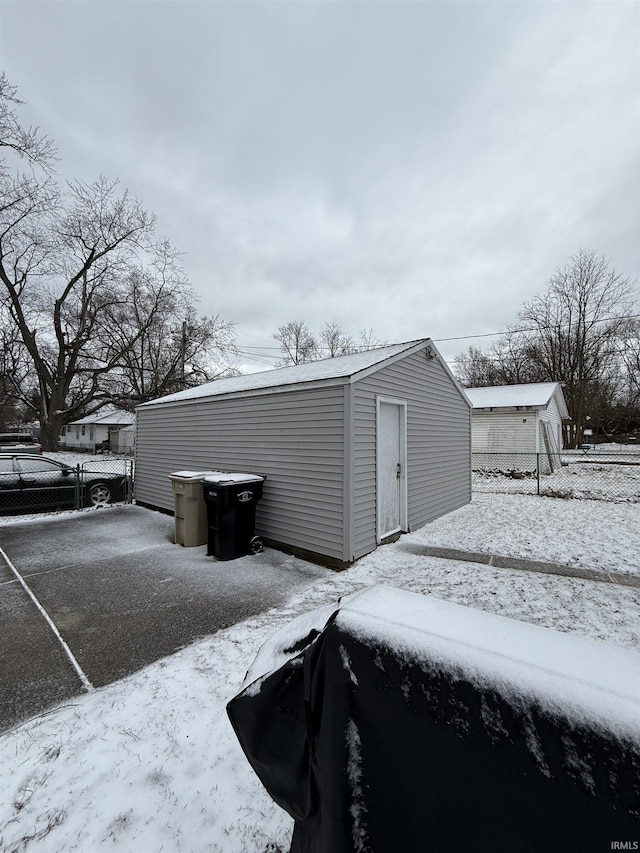 snow covered structure with fence and an outdoor structure