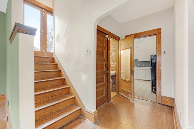 staircase featuring arched walkways, wood-type flooring, and baseboards