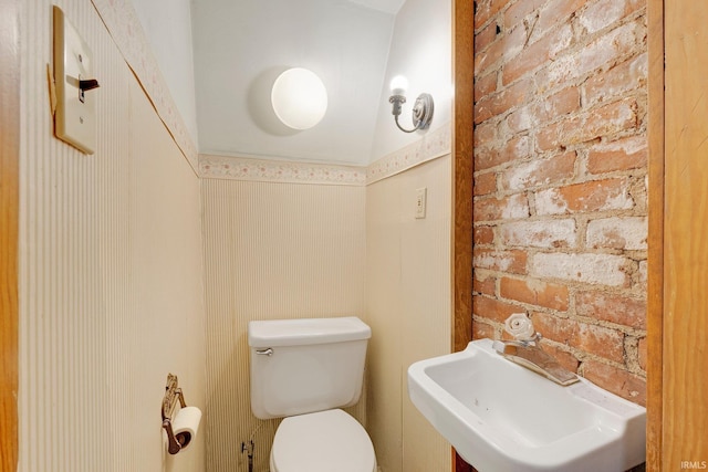 bathroom featuring brick wall, a sink, and toilet