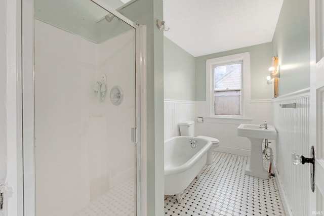 bathroom featuring toilet, a sink, a soaking tub, wainscoting, and a stall shower