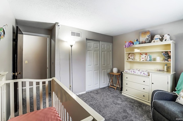 bedroom with a textured ceiling, visible vents, dark colored carpet, and a closet