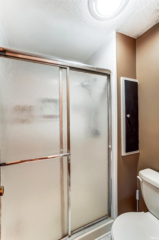 bathroom with toilet, a stall shower, and a textured ceiling