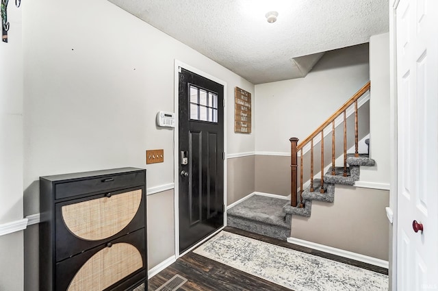 foyer entrance with visible vents, a textured ceiling, wood finished floors, baseboards, and stairs