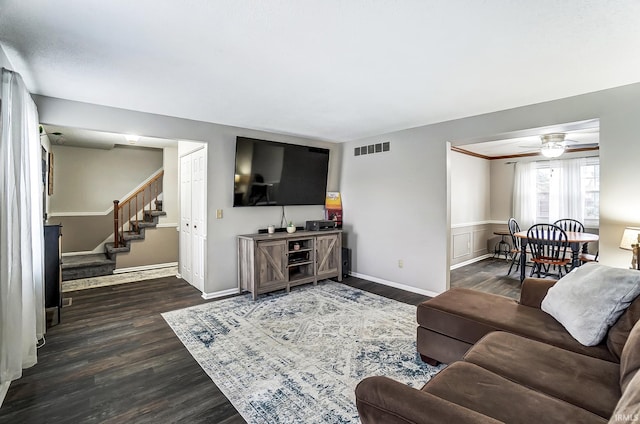 living room featuring dark wood-style flooring, visible vents, baseboards, a ceiling fan, and stairway