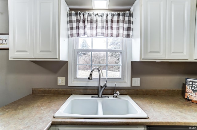 kitchen featuring dishwasher, a sink, and white cabinets