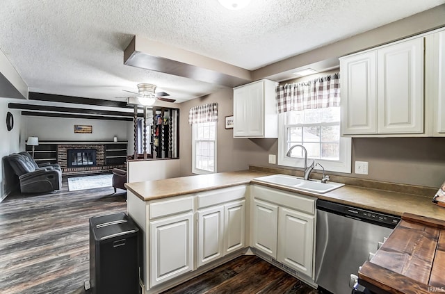 kitchen featuring a peninsula, a sink, stainless steel dishwasher, a brick fireplace, and dark wood finished floors