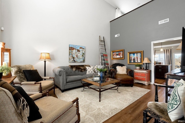 living room with visible vents, a towering ceiling, and wood finished floors