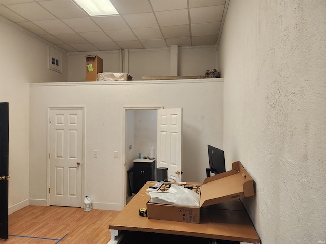 office featuring a paneled ceiling, a textured wall, baseboards, and wood finished floors