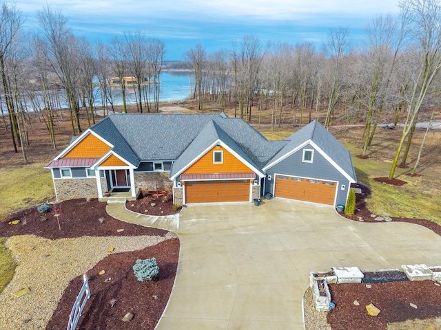 craftsman inspired home featuring an attached garage, a shingled roof, a water view, stone siding, and concrete driveway