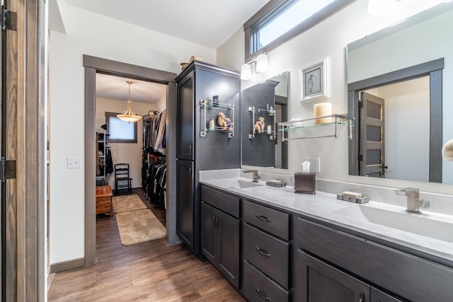 bathroom with double vanity, a sink, a spacious closet, and wood finished floors