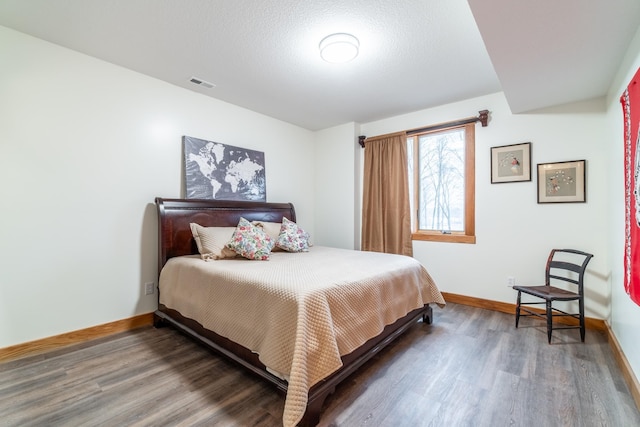 bedroom featuring visible vents, a textured ceiling, baseboards, and wood finished floors