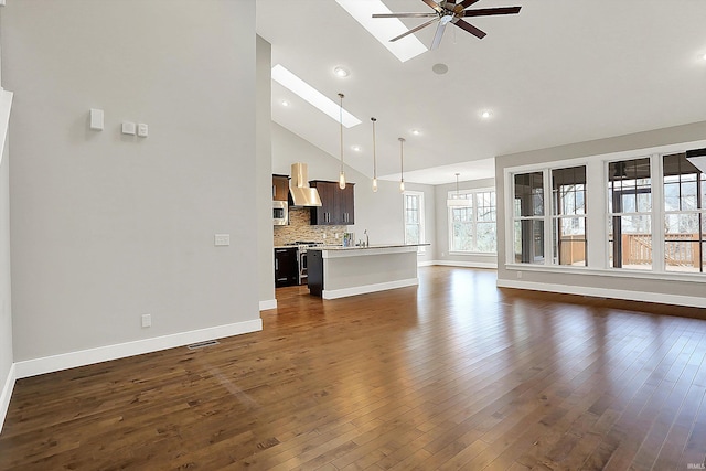 unfurnished living room featuring a skylight, dark wood finished floors, ceiling fan, high vaulted ceiling, and baseboards