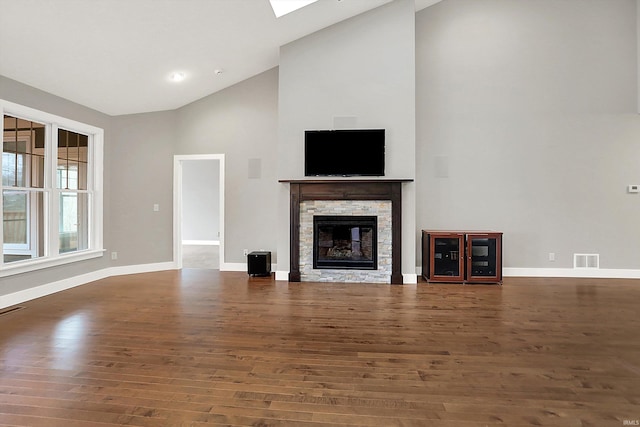 unfurnished living room with baseboards, visible vents, wood finished floors, and a stone fireplace