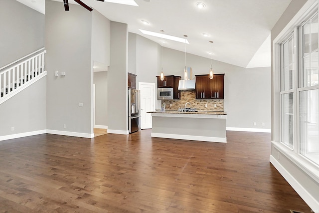 unfurnished living room featuring plenty of natural light, a skylight, dark wood finished floors, and baseboards