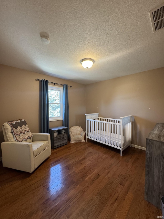 unfurnished bedroom with a textured ceiling, wood finished floors, visible vents, and baseboards