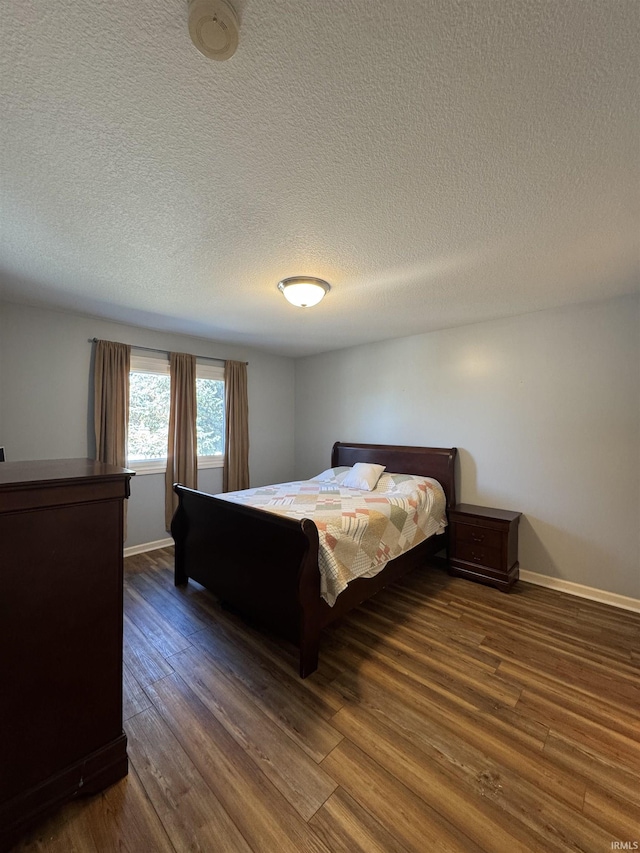 bedroom featuring baseboards, dark wood finished floors, and a textured ceiling