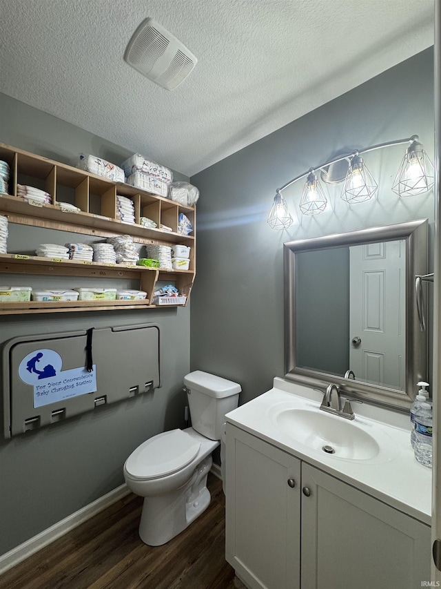 bathroom featuring a textured ceiling, toilet, wood finished floors, vanity, and visible vents