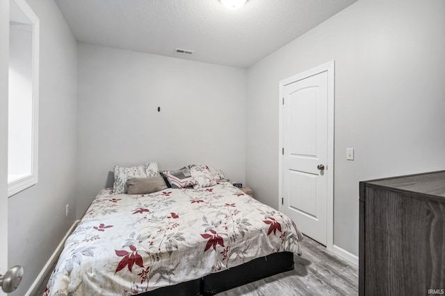 bedroom featuring a textured ceiling, wood finished floors, visible vents, and baseboards