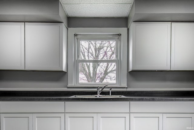 room details featuring dark countertops, a drop ceiling, white cabinets, and a sink