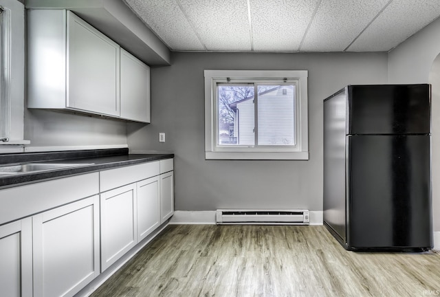 kitchen featuring a drop ceiling, dark countertops, light wood-style flooring, freestanding refrigerator, and baseboard heating