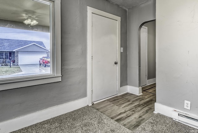 foyer with a baseboard radiator, arched walkways, baseboards, and wood finished floors