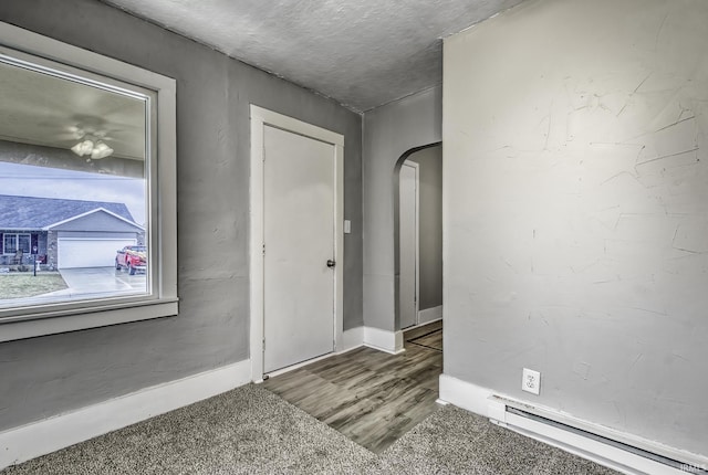 empty room with baseboards, a baseboard radiator, arched walkways, and wood finished floors