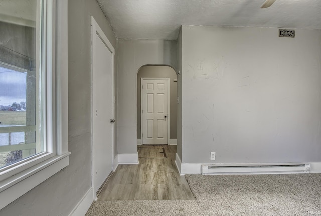 hall with arched walkways, light wood finished floors, baseboard heating, and baseboards