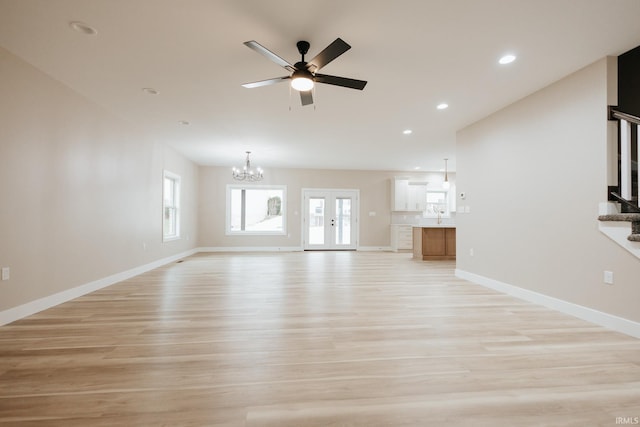 unfurnished living room with light wood finished floors, ceiling fan with notable chandelier, baseboards, and recessed lighting