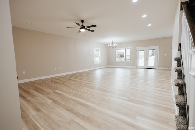 unfurnished living room with light wood-style flooring, recessed lighting, ceiling fan with notable chandelier, baseboards, and french doors