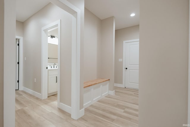 hall featuring baseboards, recessed lighting, a sink, and light wood-style floors