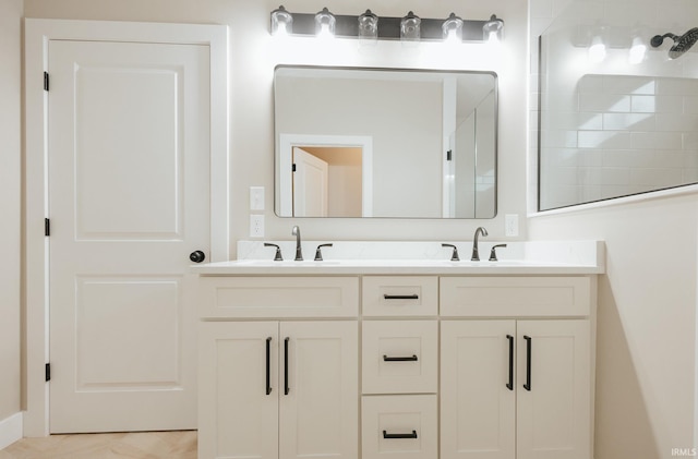 full bathroom with double vanity, tiled shower, and a sink