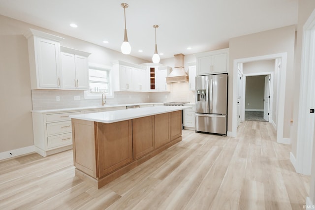 kitchen featuring tasteful backsplash, a kitchen island, stainless steel appliances, light countertops, and premium range hood