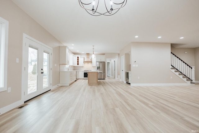 unfurnished living room featuring a sink, visible vents, baseboards, stairs, and light wood-type flooring